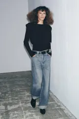 Jersey negro de punto, manga larga, con cuello redondo y detalle de pliegues o volados en la zona de los hombros.