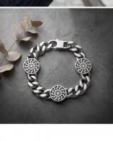 Pulsera de eslabones tipo grumet fabricada en acero, con un dije central circular que presenta un diseño grabado de rueda solar.