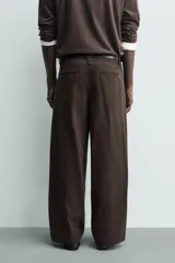 Pantalón chino de corte wide fit confeccionado en tejido de algodón. Presenta pliegues frontales, bolsillos laterales y bolsillos traseros de vivo, con cierre frontal de cremallera y botón.