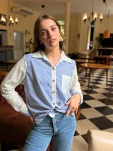 Camisa de corte clásico con diseño combinado, presenta cuerpo a rayas verticales en azul y blanco, con mangas largas y cuello en tela broderie blanca con detalles calados. Incluye bolsillo frontal en broderie y cierre central con botones.
