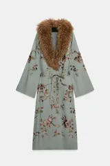 Kimono de largo midi en color verde grisáceo, con cuello de solapas amplias en pelo sintético marrón. Presenta mangas largas acampanadas y un cinturón ajustable del mismo tejido. El diseño está decorado con un delicado bordado floral en tonos tierra y rosados.