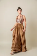 Vestido largo de fiesta con cuerpo de tul bordado en lentejuelas color cobre y falda amplia de satén en tono bronce. Presenta escote redondo, sin mangas y un lazo de satén en la cintura.