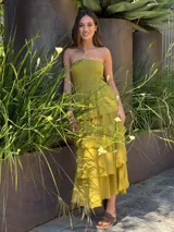 Vestido largo color crudo, sin tirantes, con cuerpo fruncido elástico tipo nido de abeja y falda de capas con volados con bordes deshilachados.