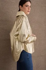 Campera de cuero metalizado color dorado con cuello de corderito sintético en tono crema. Presenta cierre frontal con botones metálicos, bolsillos frontales con solapa y diseño de corte recto.