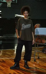 Remera de manga corta y cuello redondo, calce oversize, color marrón oscuro con efecto batik artesanal (lavado ácido). Estampa frontal con la palabra "Ravers" en estilo cursiva con contorno blanco.