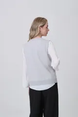 Chaleco de punto gris con escote en V, cierre frontal de botones y dos bolsillos delanteros con terminación acanalada.