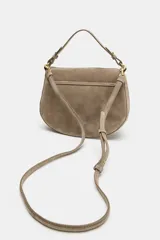 Bolso bandolera de piel gamuzada color gris topo, con solapa curva, asa de mano corta y herrajes metálicos dorados.