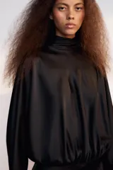 Vestido corto negro de tejido satinado, con cuello alto, mangas largas amplias y detalle de frunces en la cintura.