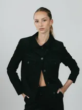 Chaqueta corta negra de pana de algodón con cuello clásico, cierre frontal con botones, dos bolsillos de parche en el pecho y mangas largas.