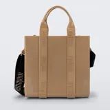 Cartera tipo tote bag Melissa modelo Dulce Bag, color tostado, fabricada en plástico PVC brillante. Cuenta con asas de mano fijas, tiras decorativas verticales con el logotipo de la marca y una correa larga ajustable y desmontable en color negro con inscripciones.