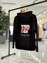 Canguro negro de corte oversize con capucha, manga larga y bolsillo tipo canguro al frente. En la espalda presenta un gran estampado gráfico con las palabras "Top Style" en blanco y rojo, acompañado de inscripciones y detalles minimalistas.