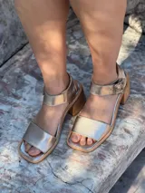 Sandalias de cuero color dorado con pulsera al tobillo y hebilla metálica. Taco bajo de madera.