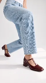 Zapatos de tacón bajo tipo Mary Jane con tira en T, confeccionados en charol color burdeos, con puntera cuadrada y cierre de hebilla lateral.