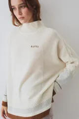 Buzo tejido de silueta amplia con cuello alto, mangas largas y puños en contraste. Presenta un diseño con franjas horizontales en el ruedo y detalles de tejido trenzado en las mangas.