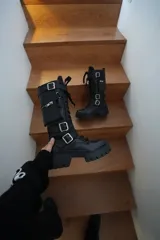 Borcegos de cuero negros, con cordones, cierre lateral y hebillas con correas ajustables. Poseen una caña de 28,5 cm de alto y una base de 4,5 cm.