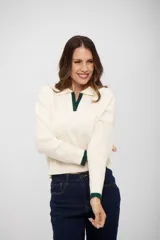 Buzo de tejido de punto color crema con cuello polo y detalles en color verde oscuro en el cuello y los puños. Presenta un diseño de manga larga con textura acanalada en los antebrazos y corte recto.
