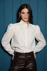 Camisa de algodón con estampado de rayas verticales finas, cuello alto con detalle de encaje broderie, cierre frontal con botones y mangas con frunces en los hombros y detalles de encaje.