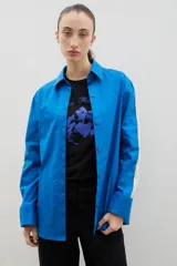 Camisa de corte holgado y largo medio, color negro con detalle de franja lateral en color crema a lo largo de las mangas. Presenta cuello clásico, cierre frontal con botones y tajos laterales en el ruedo.