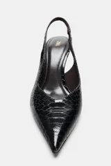 Zapato de tacón alto destalonado en color negro con acabado acharolado y textura de estampado animal. Presenta diseño de punta fina y tira elástica trasera.