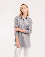 Camisa oversized con terminación metalizada color plateado, con botones a tono en delantero, largo por debajo de la cadera y tajos a los costados.