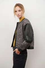 Chaqueta bomber color bordó con mangas de cuero sintético marrón y cuerpo de tweed con patrón de espiga. Cierre frontal con botones a presión y cuello redondo.