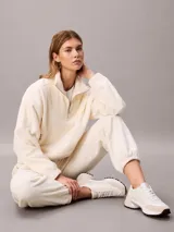 Jogger de tejido polar color blanco de Calvin Klein, con cintura elástica con cordón ajustable, bolsillos laterales con cremallera y puños elásticos en los tobillos.