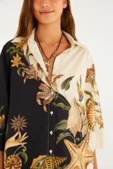 Camisa holgada de algodón con diseño bicolor (mitad negra y mitad cruda) y estampado surrealista de conchas marinas, estrellas de mar y elementos botánicos. Cuenta con cuello camisero, cierre frontal de botones y mangas anchas.