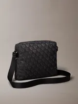Bolso cruzado rectangular de color negro con estampado de monograma en tono gris oscuro. Cuenta con correa ajustable de tela negra y un tirador de cremallera de cuero negro.
