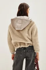 Campera de estilo híbrido con cuerpo de corderito sintético color beige y panel frontal central con cierre y capucha de tela técnica metalizada en tono grisáceo. Presenta cordones ajustables en la capucha con diseño estampado y puños con detalle de rayas.