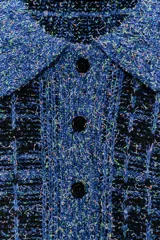 Jersey de punto con textura estructurada en tonos azules y negros, cuello polo con solapa, manga larga y cierre frontal parcial con botones.