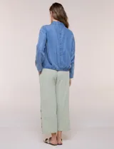 Camperita de denim liviano color azul, con cuello camisero, botones frontales ocultos, mangas largas de hombros caídos, bolsillos laterales y cordón ajustable en la cintura.