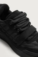 Zapatilla estilo skate color negro, con diseño de volumen, parte superior de piezas combinadas, tira adherente en el empeine y cordones gruesos. Suela con volumen y diseño irregular.