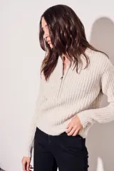 Sweater de punto color crema, con cuello redondo y cierre metálico a la mitad del frente.