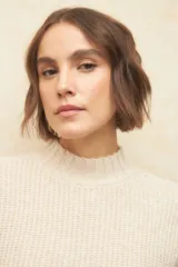 Polera de tejido de punto color beige, con cuello alto, mangas largas con puños acanalados y detalle de trenzas en los hombros.