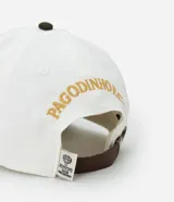 Gorra de algodón color blanco con visera curva y ajuste de hebilla de cuero marrón. Presenta bordado frontal con letras "Pagodinho F.C." en dorado.