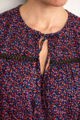 Blusa azul con estampado floral en tonos rosa y celeste, con mangas cortas, cuello redondo con abertura en forma de lágrima y detalle de encaje negro en el pecho.