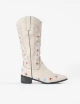 Botas estilo tejano de caña alta, confeccionadas en cuero vegano color beige. Presentan un diseño bordado con estrellas en tonos rojo, azul y gris, con taco cuadrado bajo y punta ligeramente afinada.