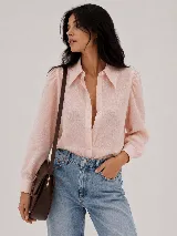 Camisa de color rosado claro con textura sutil, cuello camisero clásico y cierre frontal con botones. Presenta mangas largas con volumen en los hombros y puños con detalle de ondas.