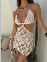 Vestido corto de crochet color crudo, estilo halter con escote profundo en V y recortes laterales. La falda presenta un patrón de tejido calado con diseño de escamas.