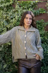 Saco tejido de punto con diseño de ochos y trenzas, color negro. Presenta cuello estilo camisero, cierre frontal con botones tipo joya, mangas holgadas y silueta oversize.