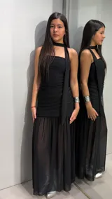 Vestido largo negro strapless con falda translúcida y detalle de bufanda o lazo integrado al cuello.