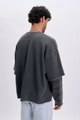 Sudadera gris oscuro de doble manga, con efecto de capas que simula una camisa a cuadros debajo, cuello redondo y bordado sutil en el pecho.