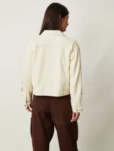 Campera de denim color off white con cuello camisero, bolsillos con solapa en el pecho y cierre frontal con botones metálicos. Presenta detalles de bordado con perforaciones en las mangas.