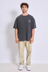 Remera de corte oversize color gris oscuro con efecto lavado, cuello redondo y manga corta. Presenta un pequeño estampado gráfico en el pecho izquierdo.