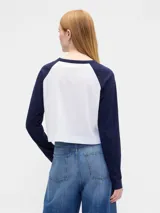 Remera de manga larga estilo raglán con cuerpo en color crema y mangas en color verde oscuro. Presenta un pequeño logo estampado en el pecho.