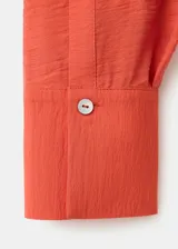 Camisa de viscosa y poliamida color rojo, con cuello camisero, manga larga y diseño cruzado con lazo ajustable en la cintura.