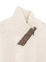 Polera tejida en lambswool color gris, con cuello alto y cierre frontal parcial con detalle en negro. Presenta diseño de tajos laterales en el ruedo, puños acanalados con detalle de rayas en contraste y un pequeño aplique circular con logo en el frente.