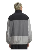 Campera deportiva Under Armour con cierre frontal completo, diseño de bloques de color en tonos negro y gris. Presenta cuello alto, bolsillos laterales con cierre y puños elásticos. Incluye tecnología UA Storm que repele el agua.