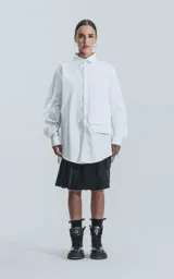 Camisa blanca de manga larga, confeccionada en poplín de algodón, con calce oversize y un bolsillo frontal asimétrico y poco convencional.