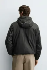 Parka de tejido técnico con acabado engomado, cuello subido y capucha ajustable. Presenta cierre frontal con cremallera oculta bajo solapa con botones a presión, bolsillos laterales de vivo y mangas largas con puños ajustables.